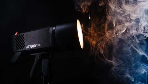 AD600Pro studio flash with warm and cool-colored smoke effects swirling around its illuminated head against black background.