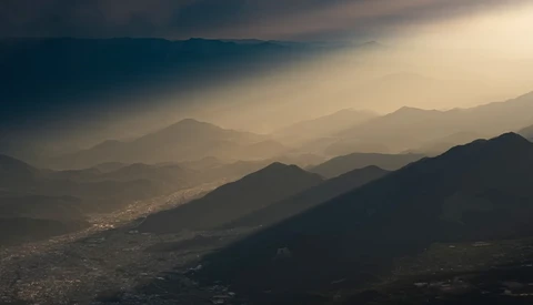 Layered mountain ranges receding into golden haze with silhouetted peaks in foreground and valley settlement visible below.