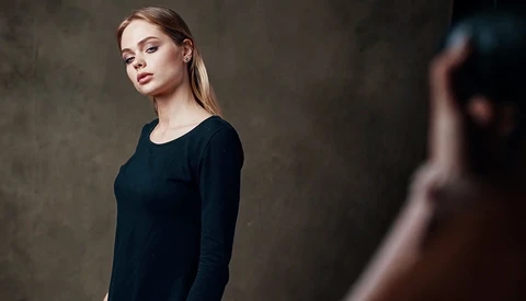 Woman in black long-sleeve shirt against textured gray background, looking toward camera.