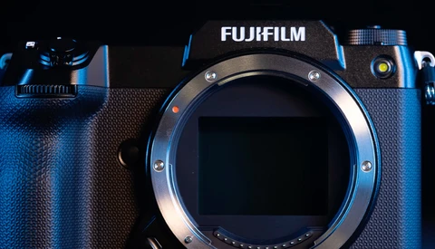 Fujifilm mirrorless camera body with lens mount exposed, front view against dark background with blue lighting.