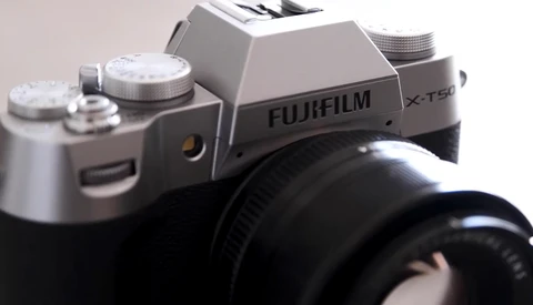 Fujifilm X-T50 mirrorless camera with silver top plate and black lens attached, shot against neutral background.