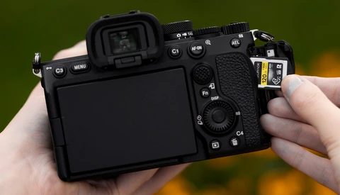 Mirrorless camera held in hands, showing rear LCD screen and control layout with various buttons and dials.
