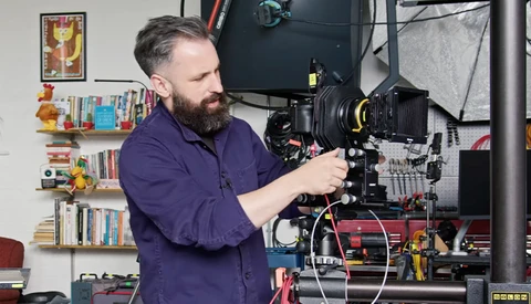 Cinematographer operating a large format film camera mounted on a rig in a studio setting.