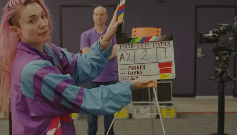 Woman with pink hair holding a colorful rainbow pride flag during a film production shoot.