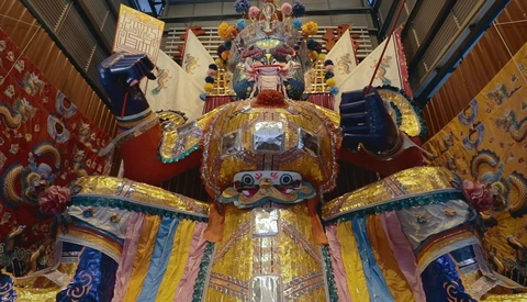 Large ornate golden statue with elaborate ceremonial dress and fierce expression displayed in a temple interior.
