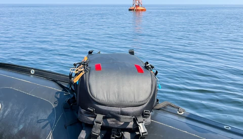 Submersible vessel mounted on a ship deck with offshore platform visible in calm blue water.