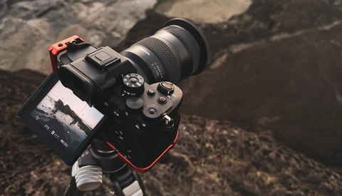 Mirrorless camera with telephoto lens mounted on tripod, displayed on rocky ground.