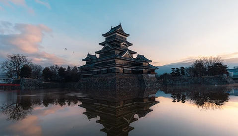 Japanese castle with tiered roofs reflected in still water at twilight.