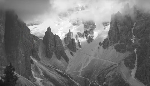 Dramatic black and white mountain landscape with towering rock formations and snow-capped peaks shrouded in clouds.