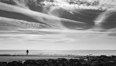 Solitary figure in wetsuit standing in shallow ocean water facing the horizon under dramatic sky.