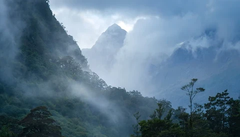 Misty mountain landscape with layered peaks shrouded in clouds and forested slopes.