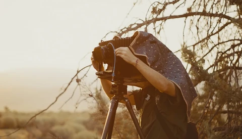 Photographer holding camera on tripod with umbrella in golden hour desert light.