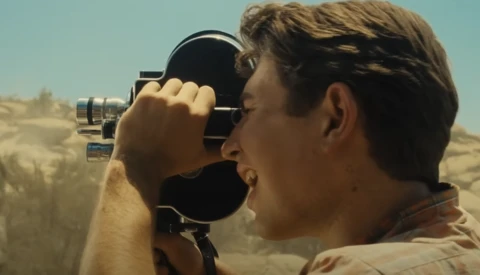 Cinematographer filming desert landscape with handheld movie camera in bright sunlight.