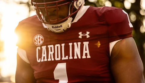 College football player in maroon uniform with Riddell helmet and Under Armour gear, photographed in golden hour sunlight.
