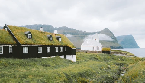 Traditional turf-roofed house with black walls and moss-covered roof overlooking coastal cliffs and mountains.