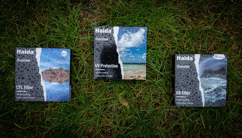 Three Haida Greyslate camera filter boxes displayed on grass, showing CPL, UV Protection, and ND Filter variants.