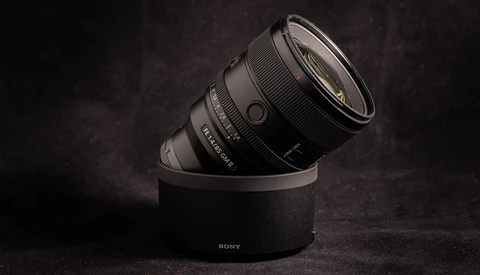 Sony lens mounted on cylindrical black stand against dark textured background.
