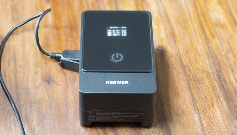 Neewer battery charger with power button and LCD display on wooden surface.