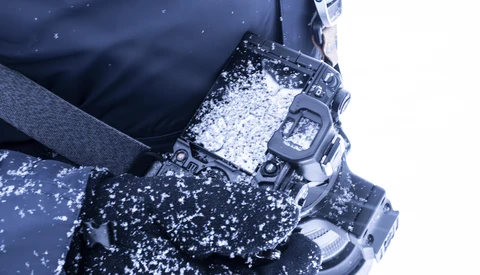Digital watch covered in snow and ice, worn on a wrist with winter gloves and dark jacket.