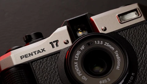 Pentax 17 film camera with red and white body and black leather grip, showing 25mm lens and built-in flash.
