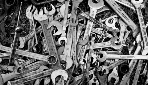 Overhead black and white arrangement of various wrenches and hand tools scattered densely across the frame.