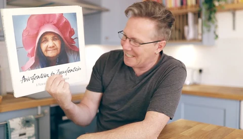 Man holding a Polaroid-style photo with handwritten caption while smiling in a kitchen.