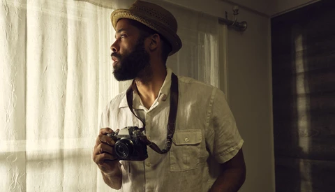 Photographer holding vintage film camera while looking out window with natural sidelight.