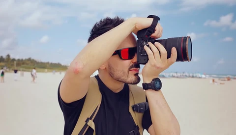 Photographer holding a DSLR camera with telephoto lens at the beach during daytime.