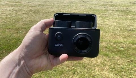 Hand holding an open Ilano compact camera against a grass background.