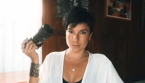 Photographer holding a telephoto lens while looking at camera in an indoor studio setting.
