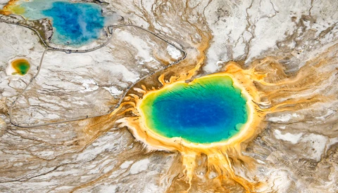 Aerial view of a geothermal hot spring with concentric rings of blue, green, and yellow mineral deposits.
