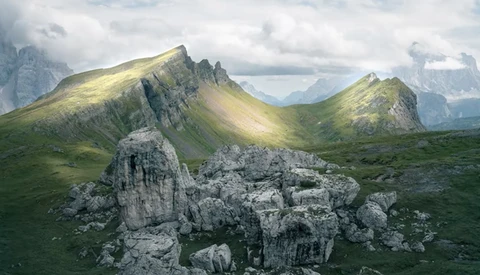 Alpine valley landscape with distinctive layered mountain peaks and weathered limestone rock formations in foreground.