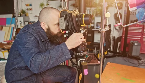 Filmmaker operating a large format movie camera mounted on a tripod in a studio workspace.