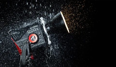 Overhead view of a camera or electronic device with water droplets and sparks creating dynamic motion effect against dark background.