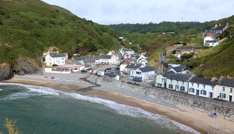 Coastal village nestled between green hills and a sandy beach with breaking waves.