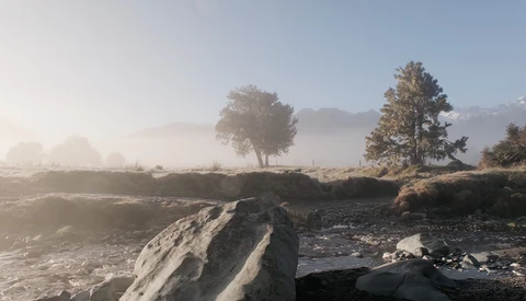 Misty landscape with trees and large boulders in foreground along a stream.