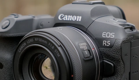 Canon EOS R5 mirrorless camera with Canon RF 50mm f/1.8 lens attached, shown in sharp focus against a blurred background.