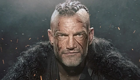 Portrait of a man with styled gray hair and facial scars against a dark background with orange light effects.