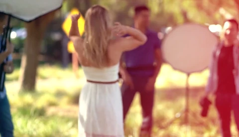 Woman in white dress dancing outdoors at an event with blurred guests and warm golden lighting.