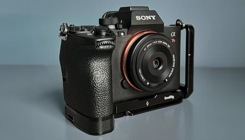 Sony Alpha mirrorless camera with attached L-bracket and prime lens on neutral background.