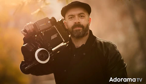 Cinematographer holding a professional cinema camera on his shoulder against a warm, golden-hour background.