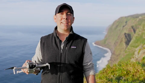 Man holding a drone while standing on a coastal cliff overlooking the ocean.