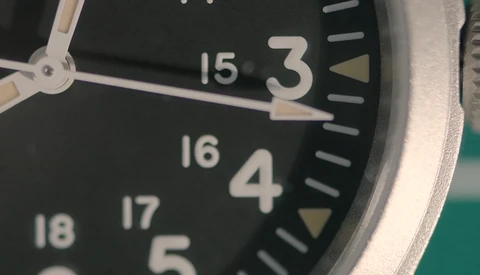 Close-up of a watch face with black dial, luminous hands, and numbered hour markers from 3 to 18.