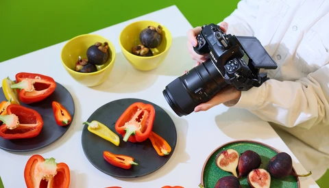 Photographer holding DSLR camera over styled food photography setup with fresh vegetables and fruits.