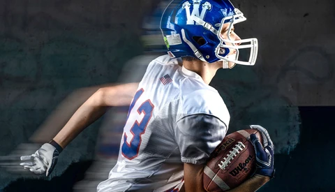 Football player in blue and white uniform holding ball with motion blur effect.