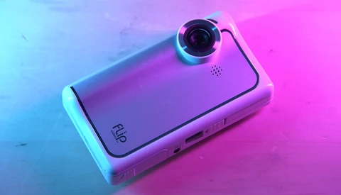 Compact camera device with prominent lens on vibrant neon blue and pink gradient background.