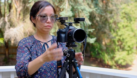 Cinematographer operating a cinema camera mounted on a tripod with follow focus gear in an outdoor garden setting.