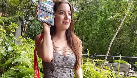 Woman holding a color reference chart outdoors while looking at camera.