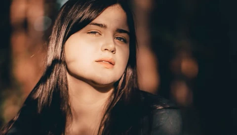 Young woman with long dark hair gazing upward in warm golden light against a dark background.