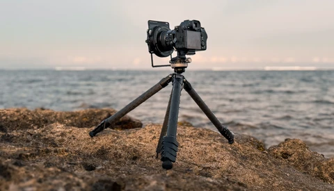 Professional camera mounted on tripod positioned on rocky beach overlooking calm ocean at sunset.